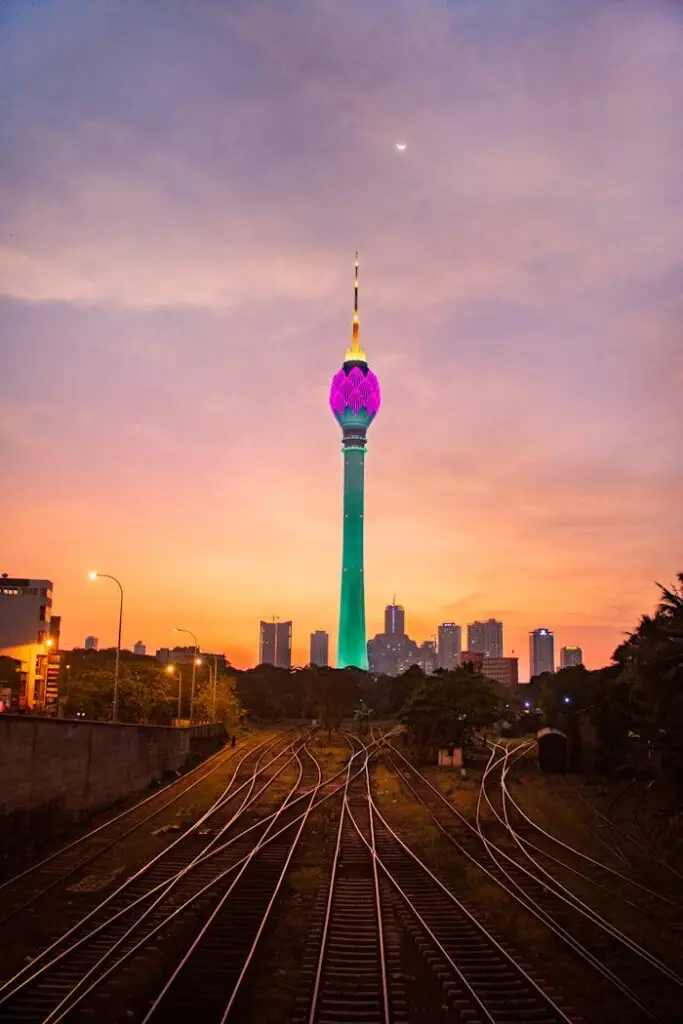 View of illuminated Colombo Lotus Tower at sunset with railway foreground in Sri Lanka.