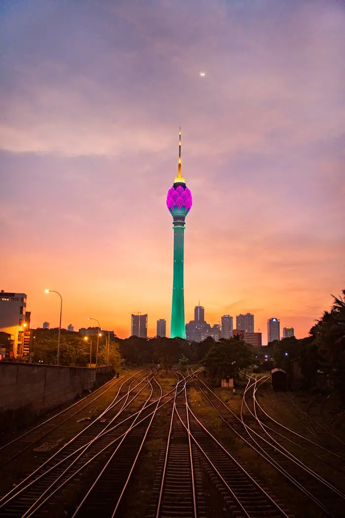 View of illuminated Colombo Lotus Tower at sunset with railway foreground in Sri Lanka.